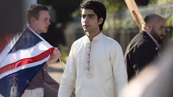 Javed (Viveik Kalra) stands in traditional clothing between men holding flags