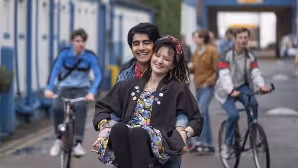 Javed (Viveik Kalra) carries Eliza (Nell Williams) along a street as cyclists pass