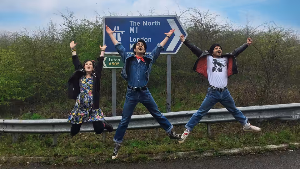 Three young people leap beside a motorway sign pointing toward London