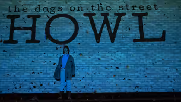 A lone figure stands beneath large HOWL lettering on a brick wall