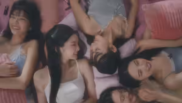 A group of young women lounge together on pink bedding, smiling and laughing