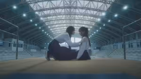 Two young women in school uniforms kneel facing each other on an indoor sports court