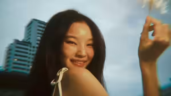 A young woman smiles toward the camera outside, with high-rise buildings behind her