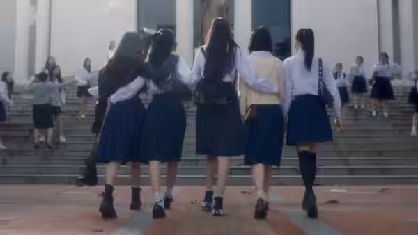 Schoolgirls in uniforms walk arm in arm up the broad steps toward their school