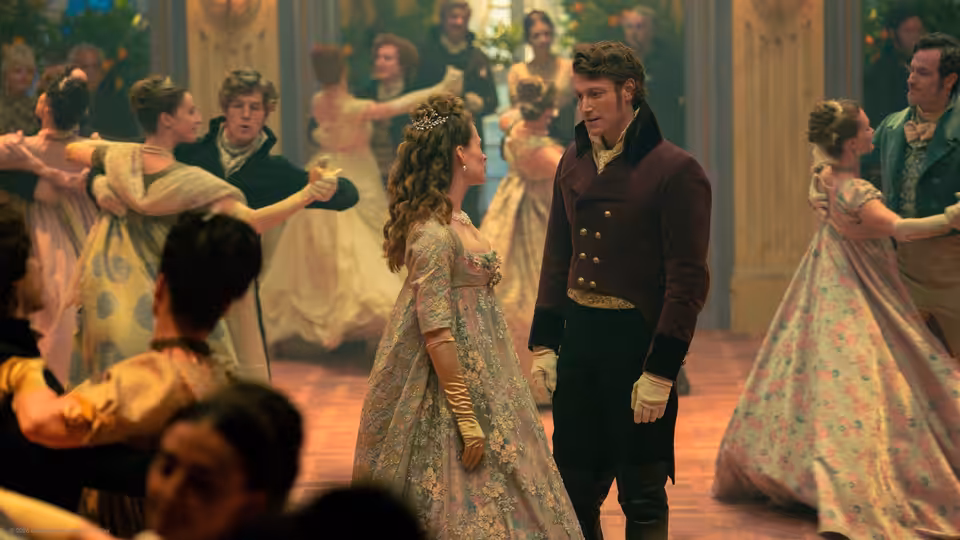 A woman in a patterned gown faces a uniformed man as couples dance in a ballroom