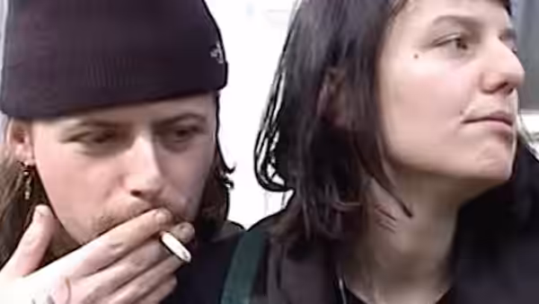 A person in a beanie smokes beside a long-haired companion