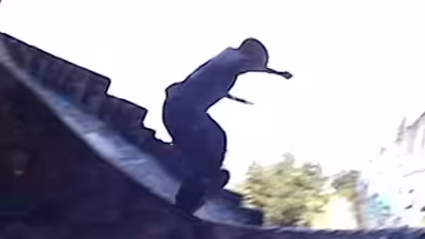 A silhouetted person crouches on the edge of a rooftop above the street