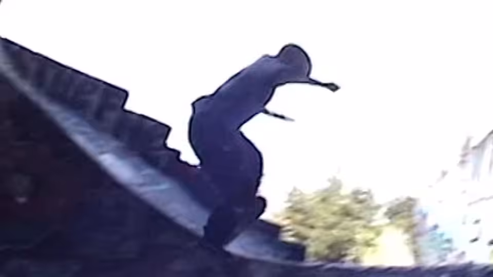 A silhouetted person crouches on the edge of a rooftop above the street