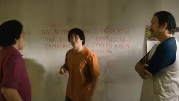 Three men stand talking beside handwritten words on a room wall