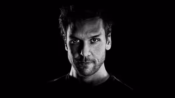 Dane Cook, appearing as himself, faces the camera against a black background