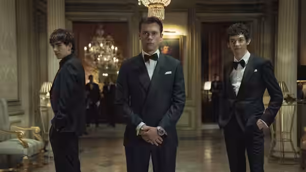 Three young men in tuxedos pose in an elegant mansion hallway