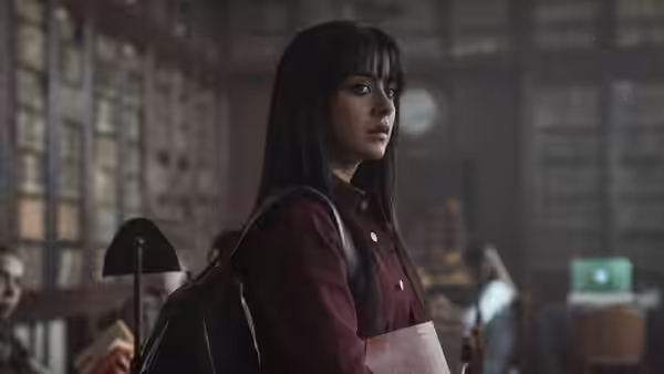 Jude Derry (Irene Balmes) stands in a library holding a folder
