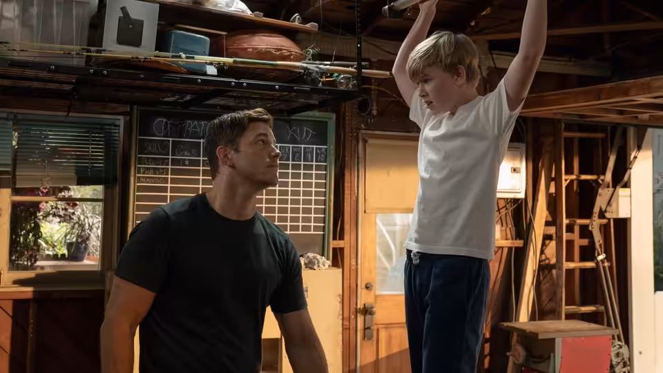 Jake (Chris Pratt) watches a boy hang from an overhead bar in a garage