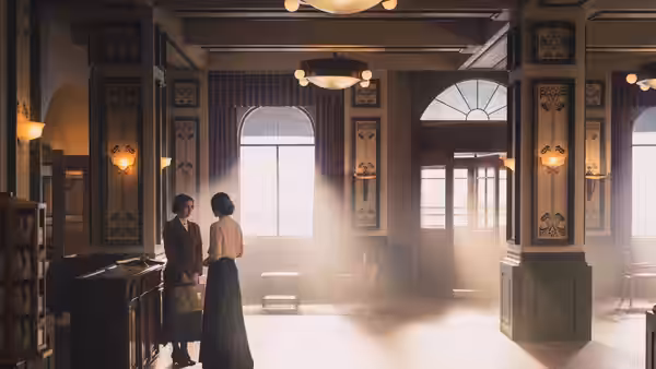 Two women stand beside the reception desk in a sunlit hotel lobby