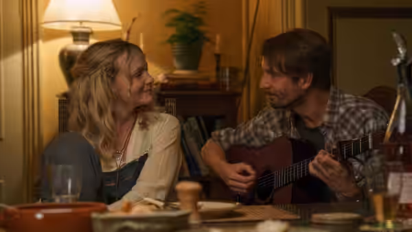 Nell Mortimer (Carey Mulligan) smiles at Herb McGwyer (Tom Basden) playing guitar indoors
