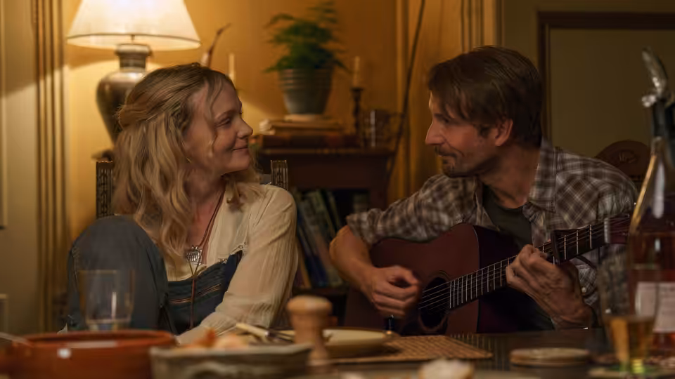 Nell Mortimer (Carey Mulligan) smiles at Herb McGwyer (Tom Basden) playing guitar indoors