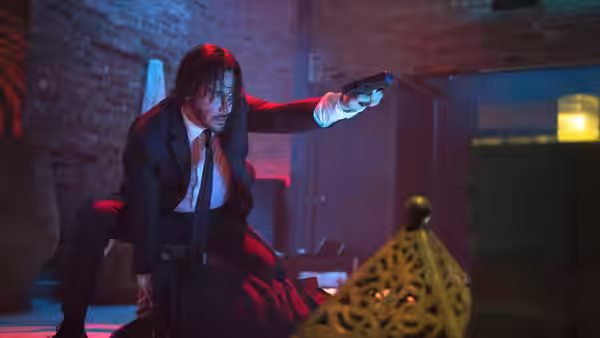 John Wick (Keanu Reeves) kneeling and pointing a gun over a man