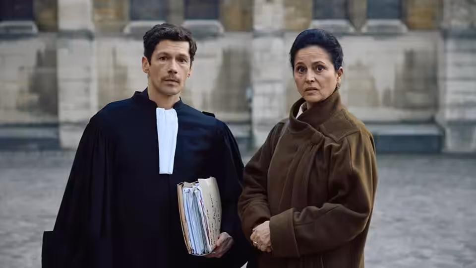 A lawyer holding papers stands beside a woman outside a stone courthouse