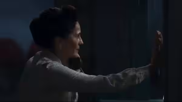 A woman reaches toward a bloody handprint on a glass pane