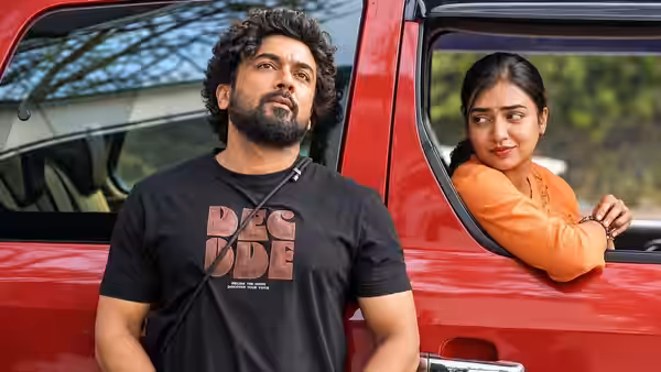 A curly-haired man stands beside a red vehicle as a woman leans from its window