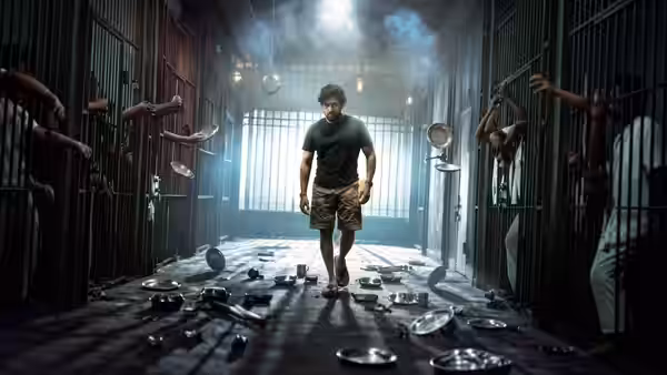 A curly-haired man walks through a prison corridor as inmates reach through cell bars