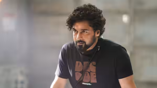 A curly-haired man in a black T-shirt leans forward intently