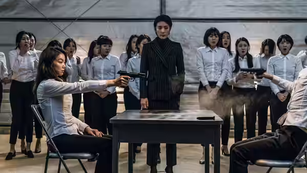 A seated woman aims a pistol as other women watch in a training room