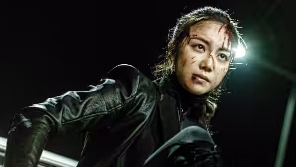 A bruised woman crouches in a black leather jacket beneath a harsh light