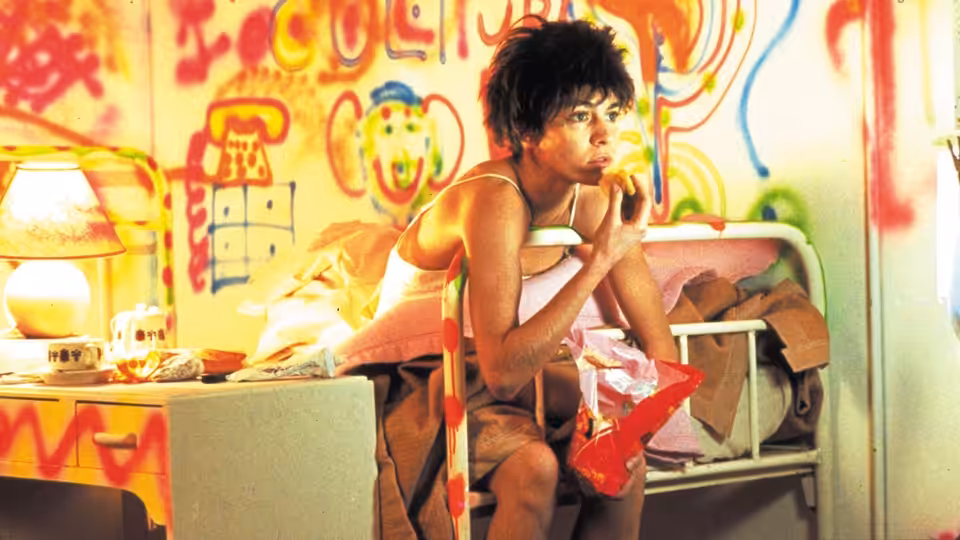 Nikita (Anne Parillaud) eating a sandwich on a bed in a graffiti-covered room