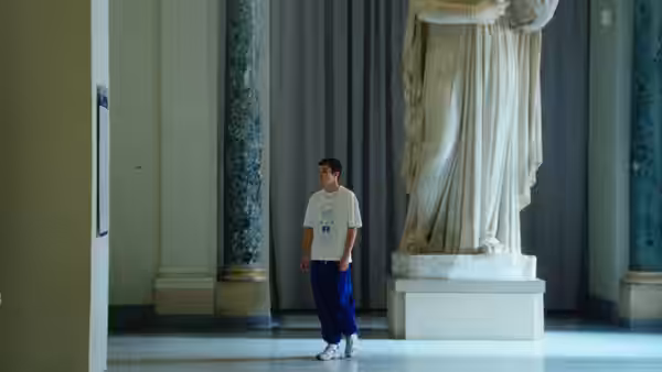 A young man stands beside a towering marble statue in a museum gallery