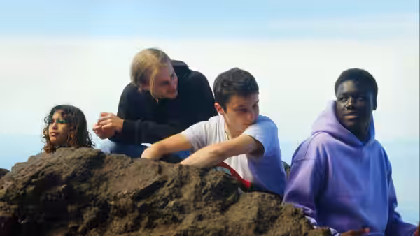 Four young people gather behind a rocky ledge overlooking the water