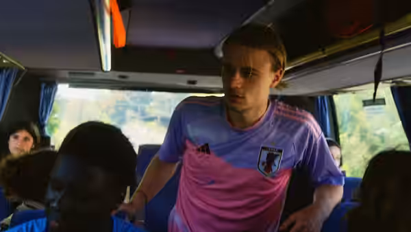 A young man in a football jersey stands in the aisle of a crowded bus