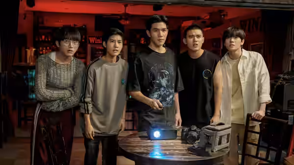 Five young people gather around a projector on a table in a red-lit room