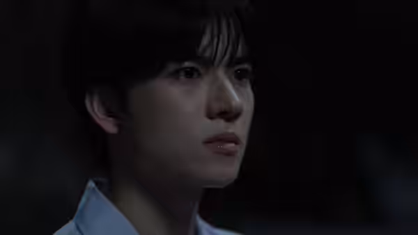 A schoolboy in a white uniform looks intently toward someone offscreen
