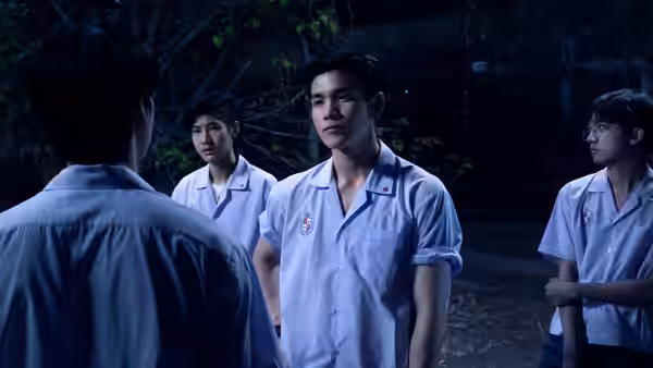 Three schoolboys face a classmate in a white uniform in a dark wooded area