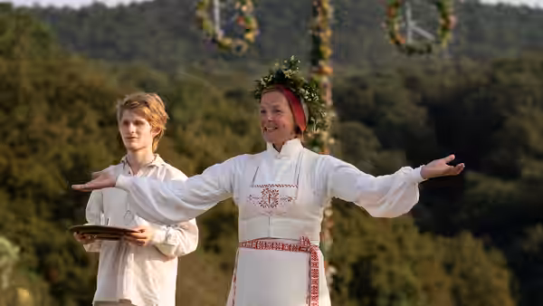 a woman in white folk costume with arms outstretched outdoors