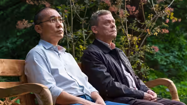 Tony Leung and a gray-haired man sit together on a garden bench