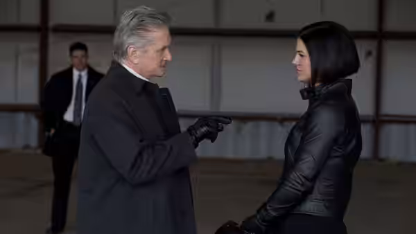 A man in a dark coat pointing at Mallory Kane (Gina Carano) inside a warehouse