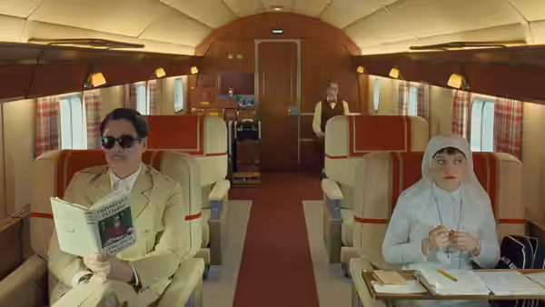 Zsa-zsa Korda (Benicio del Toro) reading aboard an airplane beside Sister Liesl