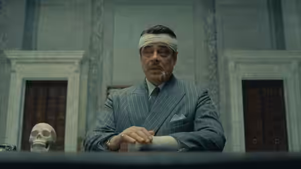 Zsa-zsa Korda (Benicio del Toro) seated at a desk with a skull
