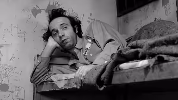 A man lies on a prison bunk with his head on his hand