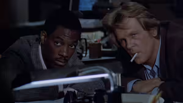 Reggie Hammond (Eddie Murphy) and Jack Cates (Nick Nolte) peer over a desk