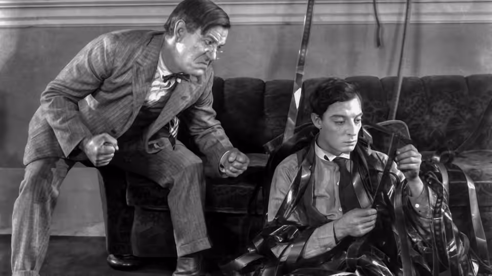 Buster Keaton seated on couch as older man leans over him