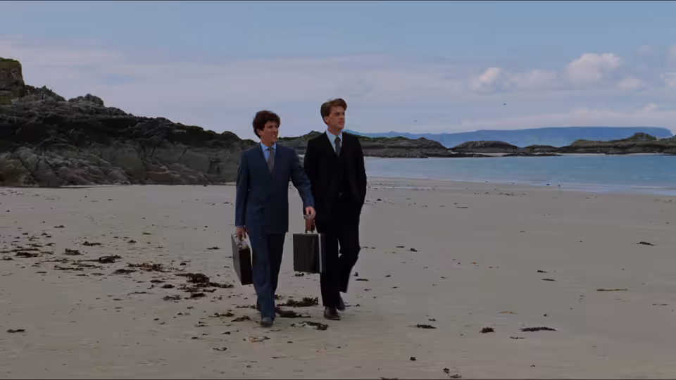 Two suited men with briefcases walking along an empty beach