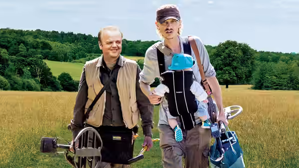 Lance (Toby Jones) and Andy (Mackenzie Crook) walking in a field with a baby