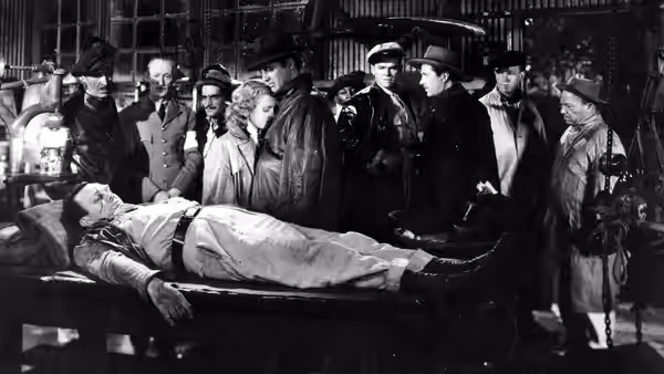 Men gather around an injured man lying on a stretcher indoors