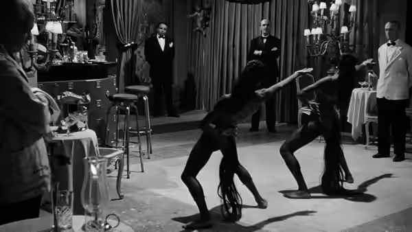 Two contortionists perform before an audience in a curtained room