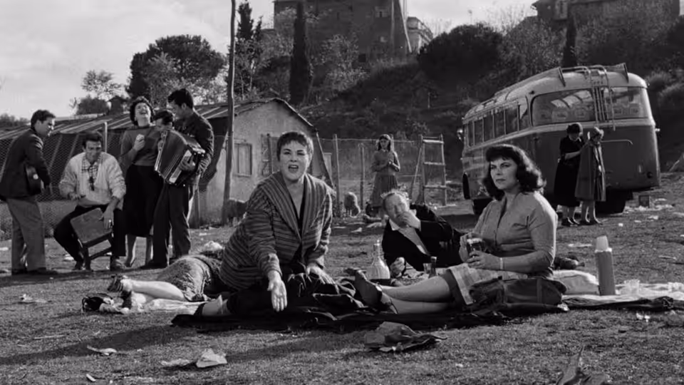 People gather beside a camper van as a woman sits among them on the ground