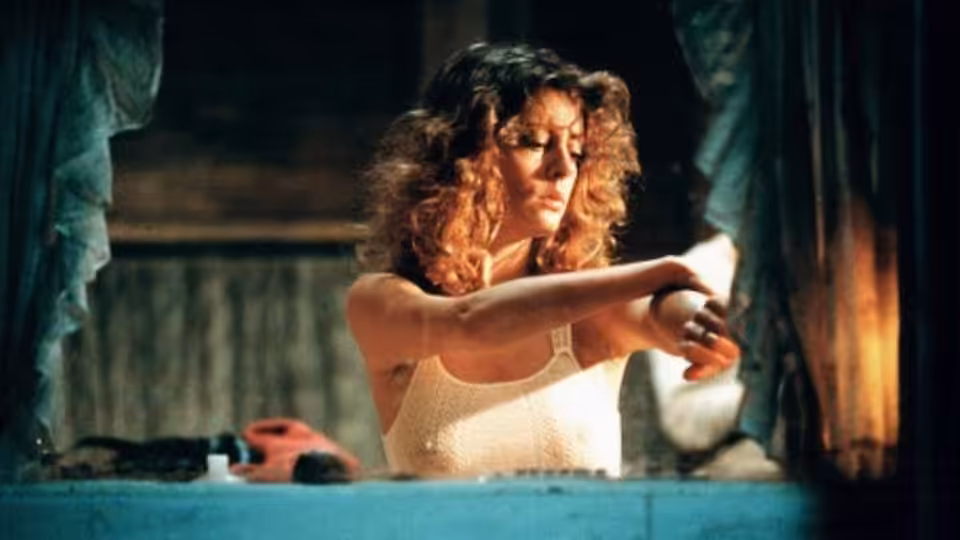 Sally (Susan Sarandon) leaning forward with arms crossed on a blue surface