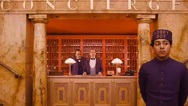 Zero (Tony Revolori) standing in front of the hotel concierge desk